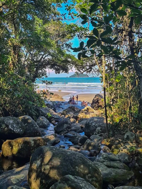 Turistas se banhando no riacho na Praia do Arpoador com o mar e a Ilha do Guarau ao fundo.