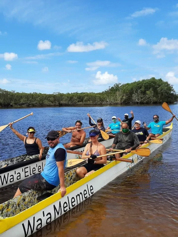 Grupo de turistas remando uma Canoa Havaiana Catamarã no Rio Itanhaém em um dia ensolarado.