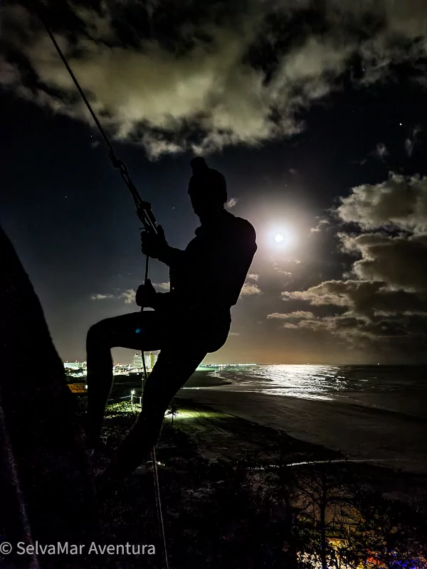 Turista desdendo o Rapel da Lua com a lua cheia e o mar ao fundo na Praia do Costão em Peruíbe.